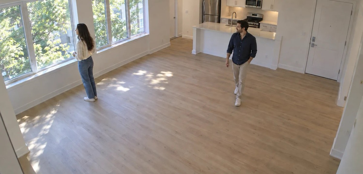 Two people touring an empty living room, seen by the camera